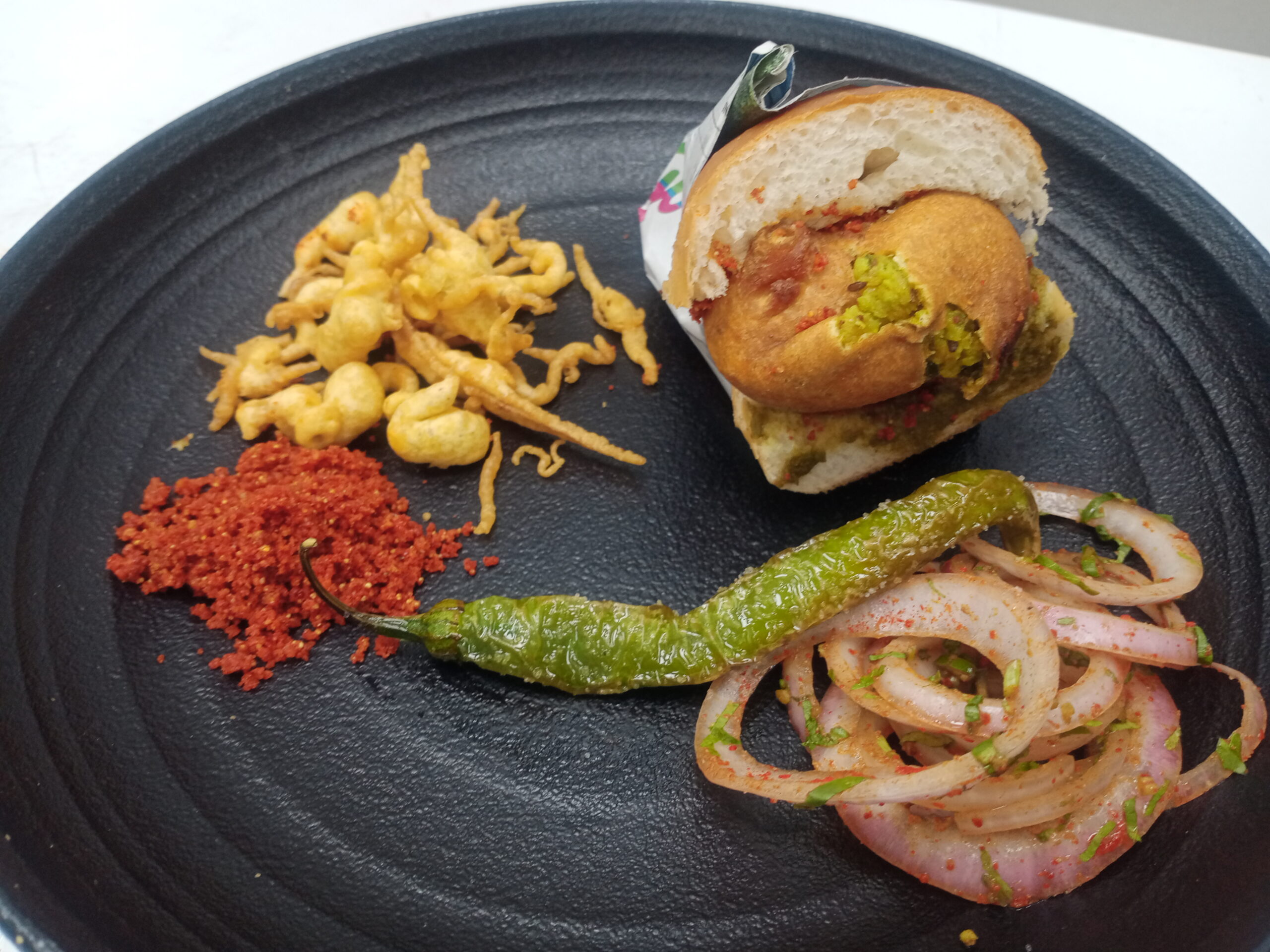 Traditional vada pav with fried chilli and spiced onions — Mumbai street food classic